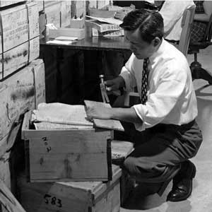 Black and white photo of Eugene Wu unboxing crates containing a shipment of documents, 1950s.
