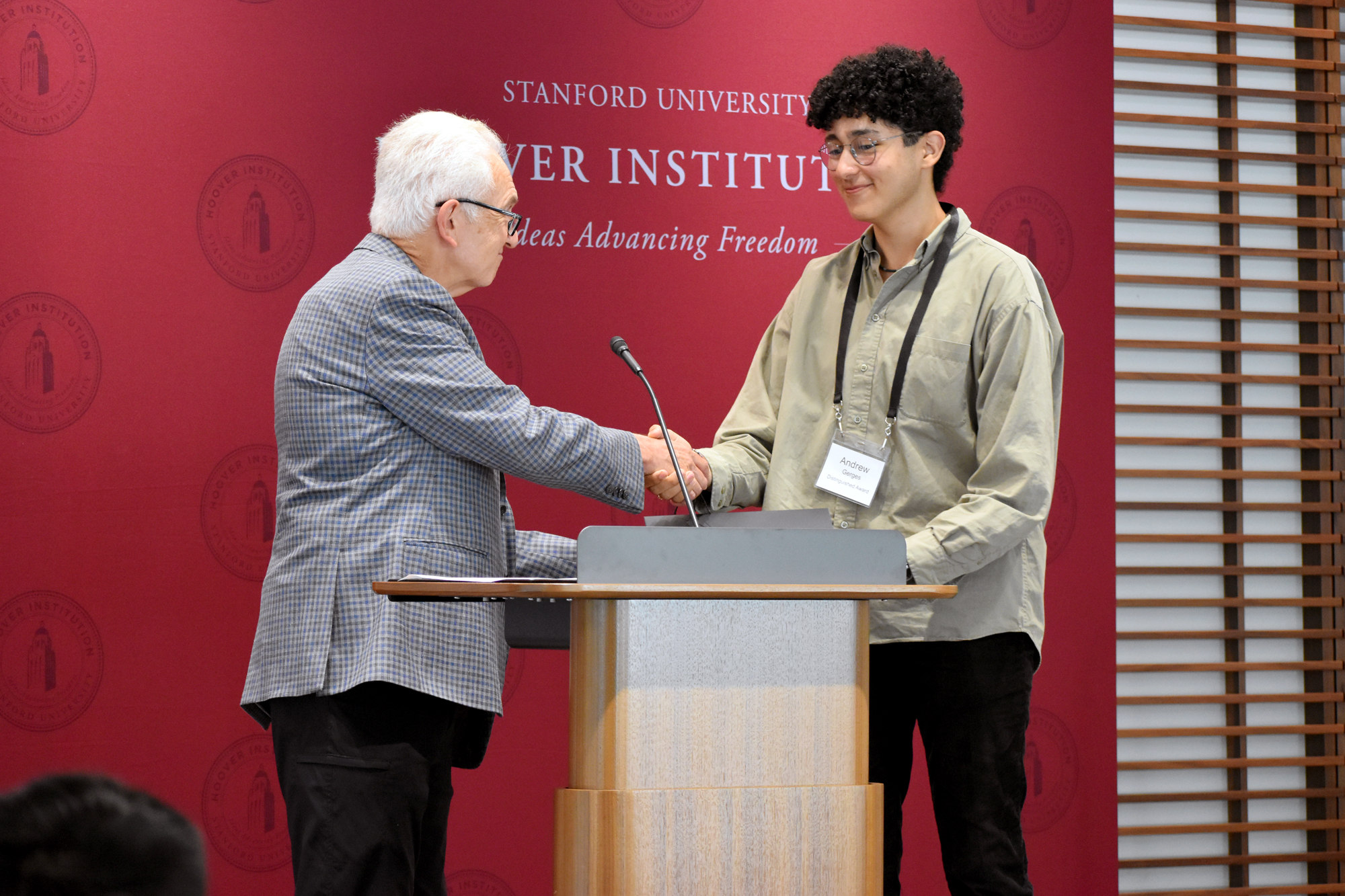 Senior Fellow Russell A. Berman congratulates Andrew Gerges, one of four winners of the 2024 Distinguished Undergraduate Essay Competition, in Shultz Auditorium on October 15, 2024. 