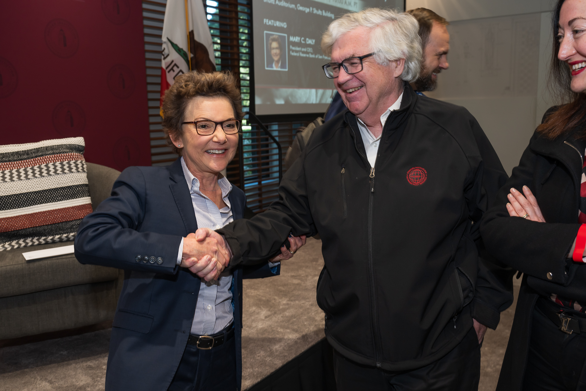 SF Fed President and CEO Mary C. Daly shakes hands with Senior Fellow John B. Taylor in Shultz Auditorium on December 6, 2024. (Steve Castillo)