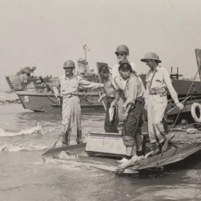 Black and white photo of US military on boats and ships in the background