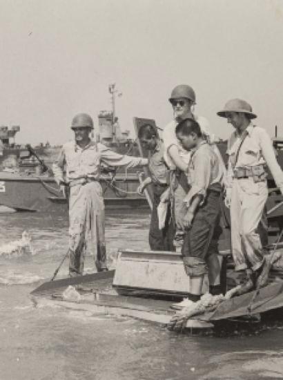 Black and white photo of US military on boats and ships in the background