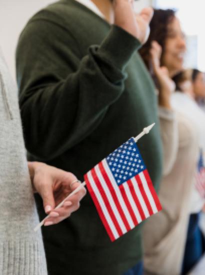 The group of multiracial people stand and raise their hand to say the pledge.