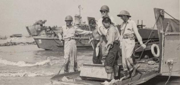 Black and white photo of US military on boats and ships in the background