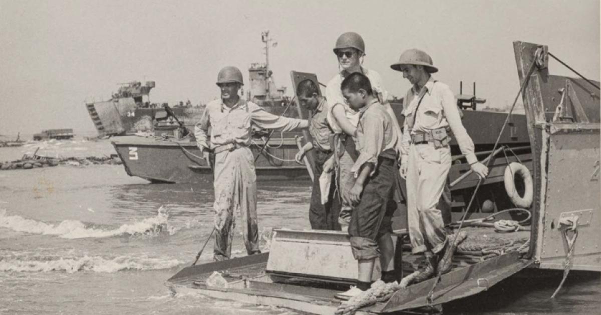 Black and white photo of US military on boats and ships in the background