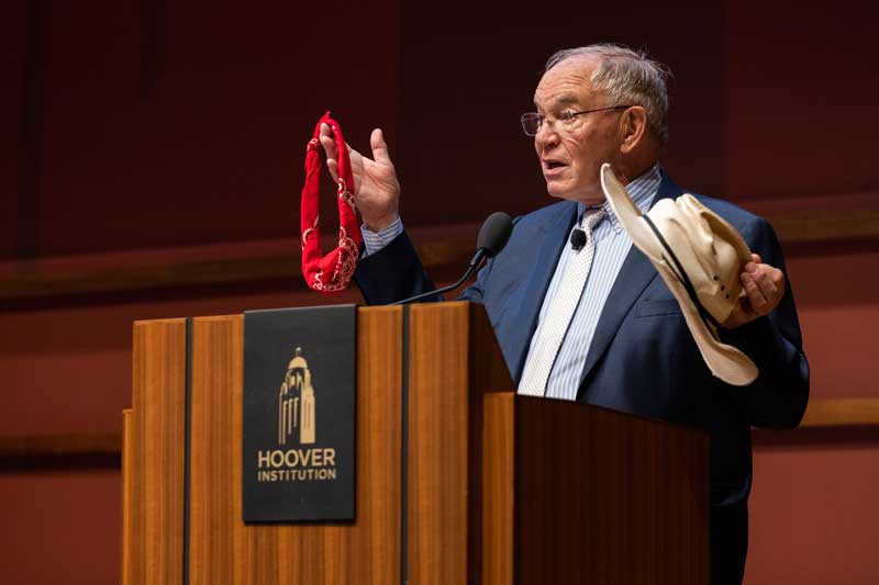 Terry Anderson introduces the Markets vs. Mandates conference on April 8, 2024, using his rancher hat and a bandanna to describe differing views of ranchers versus environmentalists on reintroducing the wolf to pasturelands.